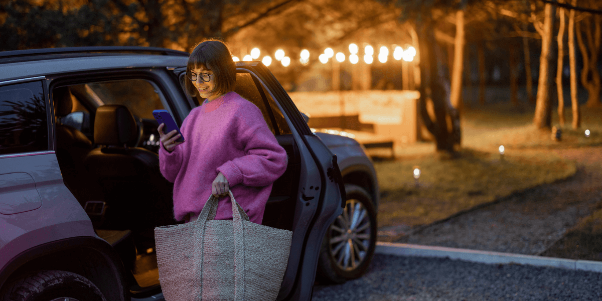 A woman in a pink shirt using her mobile phone while standing besides the car.