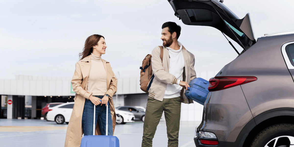 A man loading luggage into the car while a girl stands beside him, holding a suitcase, ready for their trip.