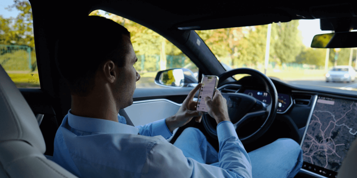 A Man sitting on driving seat and controls the car through mobile phone